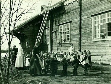 Lapsia ja lastentarhaopettajia piirileikissä Ainolan lastentarhan pihalla 1910-luvulla. Kuvan lähde on Wikipedia artikkeli tästä aiheesta.